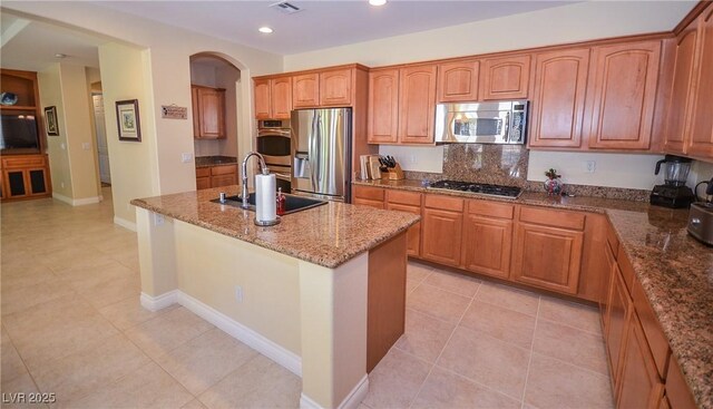 kitchen featuring sink, light tile patterned floors, appliances with stainless steel finishes, a kitchen island with sink, and stone countertops