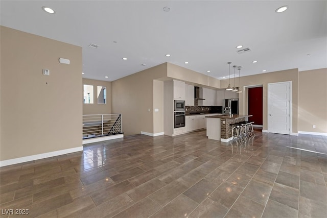 kitchen with a breakfast bar, hanging light fixtures, stainless steel appliances, white cabinets, and a center island with sink