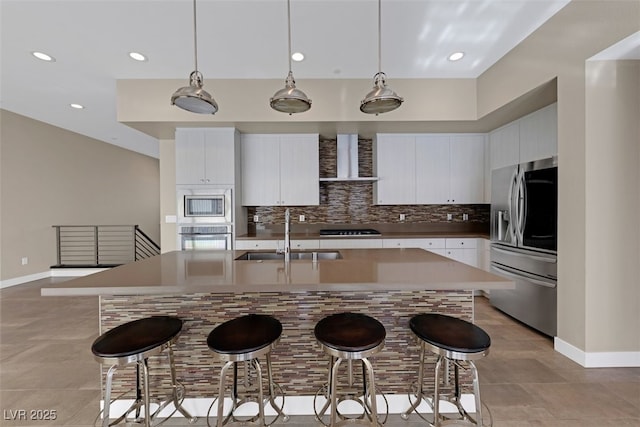 kitchen with pendant lighting, sink, wall chimney range hood, appliances with stainless steel finishes, and white cabinets