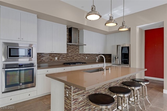 kitchen with wall chimney exhaust hood, a breakfast bar, pendant lighting, stainless steel appliances, and a kitchen island with sink