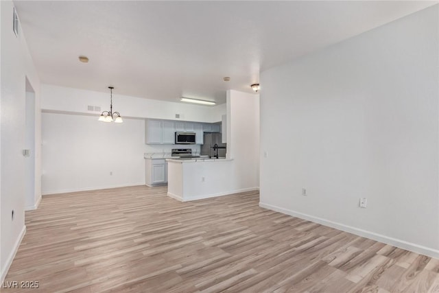 unfurnished living room featuring an inviting chandelier and light hardwood / wood-style flooring