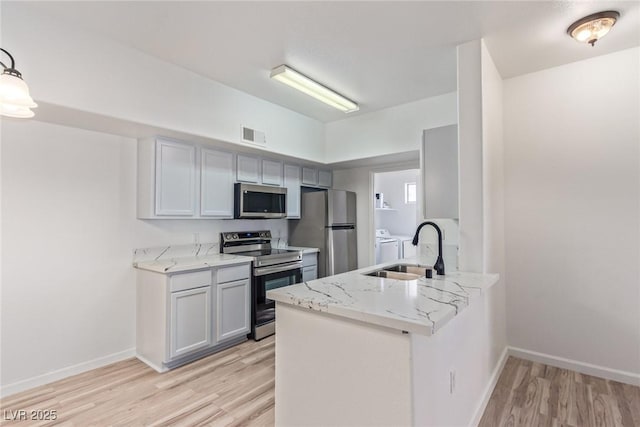 kitchen with light wood-type flooring, sink, washer and clothes dryer, and appliances with stainless steel finishes