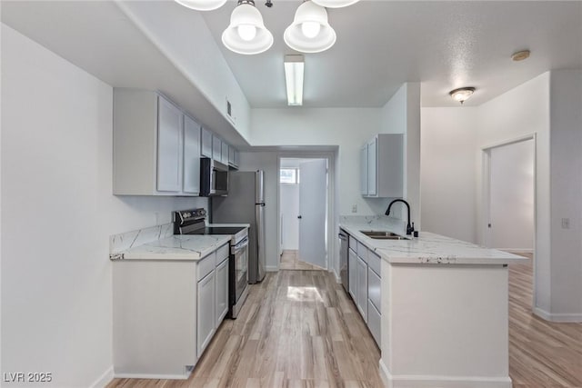 kitchen with sink, hanging light fixtures, light wood-type flooring, kitchen peninsula, and stainless steel appliances