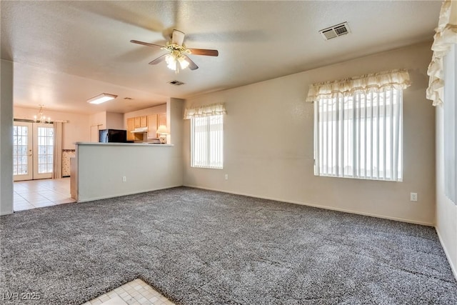 unfurnished living room with ceiling fan with notable chandelier, plenty of natural light, light colored carpet, and a textured ceiling