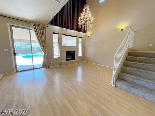 unfurnished living room with a high ceiling, a chandelier, and light hardwood / wood-style floors