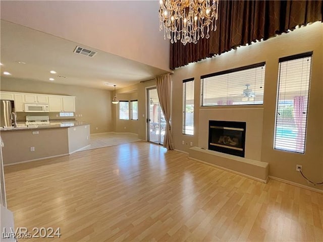 unfurnished living room with a tiled fireplace, an inviting chandelier, and light wood-type flooring