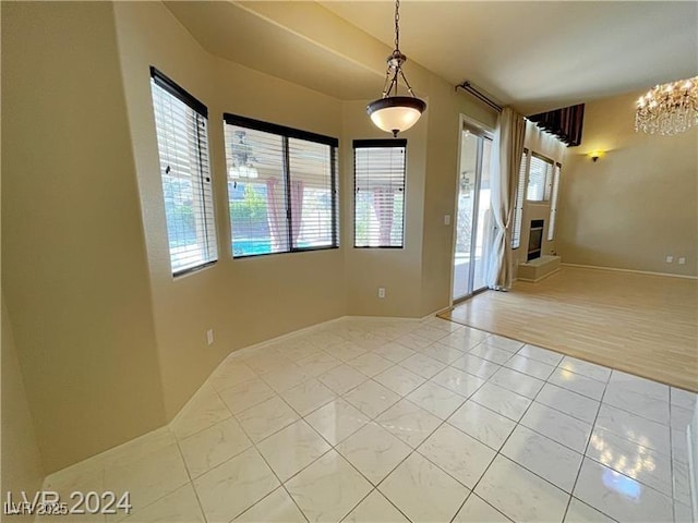 spare room with an inviting chandelier, light tile patterned flooring, a glass covered fireplace, and a healthy amount of sunlight