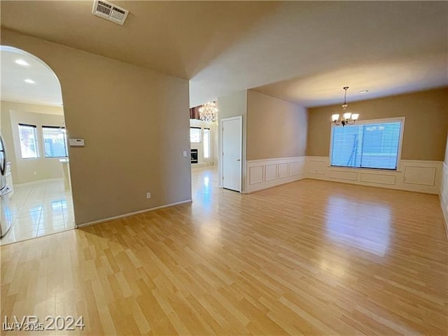 unfurnished room with an inviting chandelier, arched walkways, light wood finished floors, and visible vents