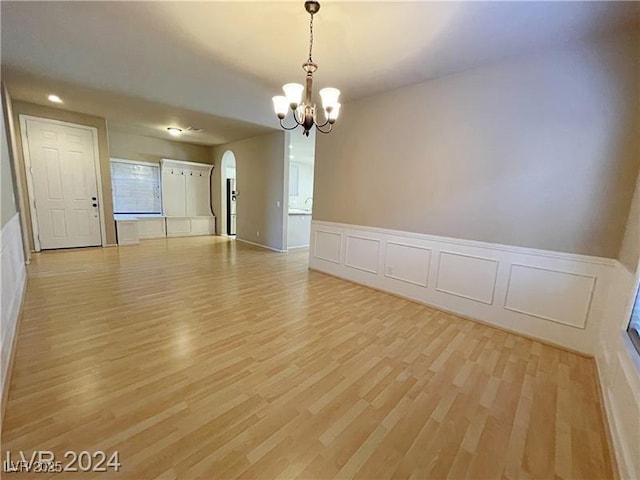 empty room featuring arched walkways, an inviting chandelier, and light wood-type flooring