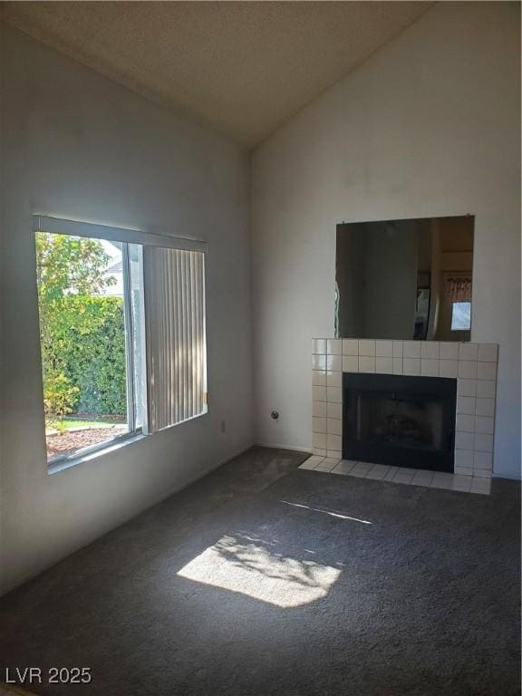 unfurnished living room with a tiled fireplace, lofted ceiling, and carpet