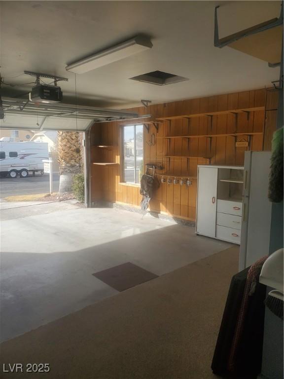 garage featuring a garage door opener, wood walls, and white fridge