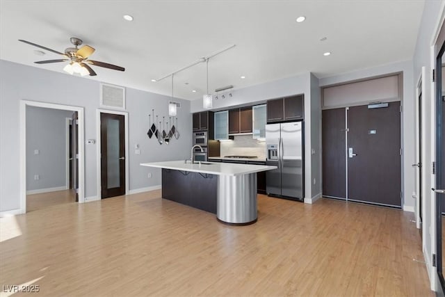 kitchen with pendant lighting, an island with sink, a kitchen breakfast bar, stainless steel refrigerator with ice dispenser, and dark brown cabinets