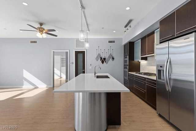 kitchen featuring appliances with stainless steel finishes, sink, dark brown cabinets, a center island with sink, and light hardwood / wood-style flooring