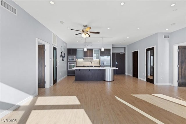 kitchen with sink, hanging light fixtures, a center island with sink, appliances with stainless steel finishes, and light hardwood / wood-style floors