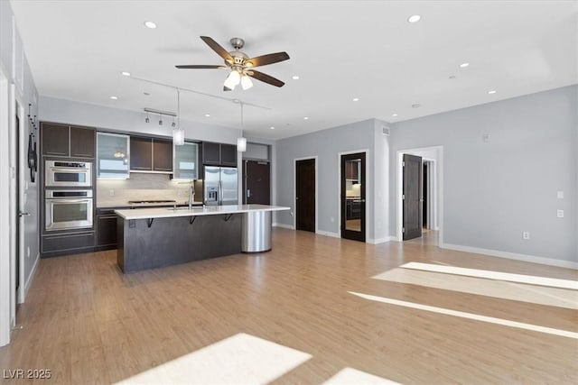 kitchen with appliances with stainless steel finishes, pendant lighting, sink, a kitchen breakfast bar, and a kitchen island with sink