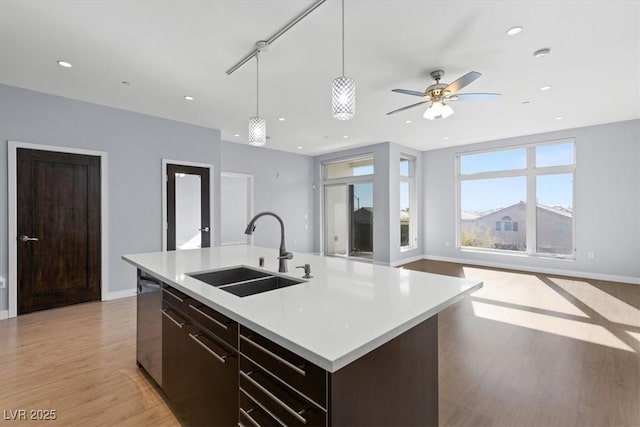 kitchen with an island with sink, dishwasher, sink, hanging light fixtures, and light hardwood / wood-style floors