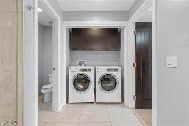 clothes washing area with cabinets, light tile patterned flooring, and washer and clothes dryer