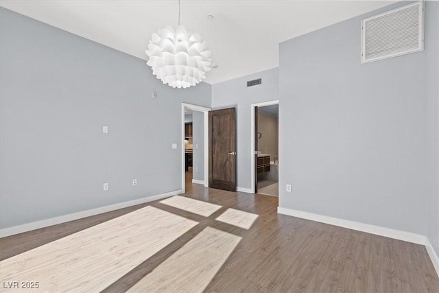 spare room with an inviting chandelier and hardwood / wood-style floors