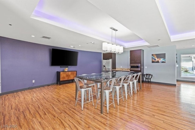 dining area featuring a raised ceiling and light wood-type flooring