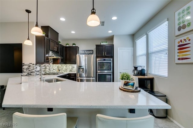 kitchen with a breakfast bar, backsplash, stainless steel appliances, decorative light fixtures, and kitchen peninsula