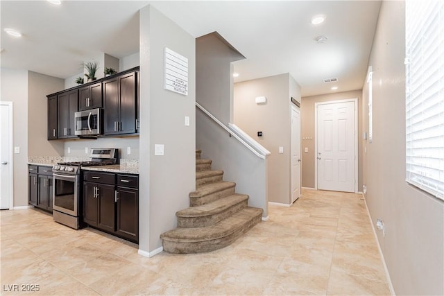 interior space featuring visible vents, baseboards, appliances with stainless steel finishes, light stone countertops, and dark brown cabinets