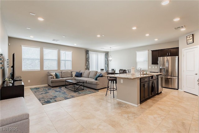 kitchen with visible vents, an island with sink, open floor plan, stainless steel appliances, and a kitchen bar