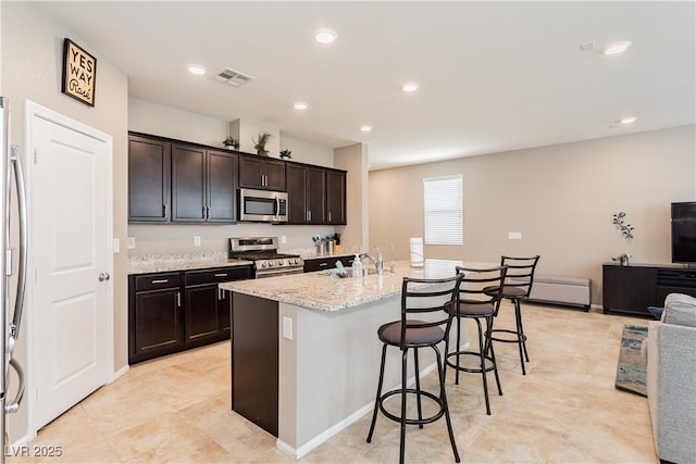 kitchen featuring stainless steel appliances, visible vents, open floor plan, an island with sink, and a kitchen bar