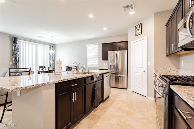 kitchen with a breakfast bar area, stainless steel appliances, visible vents, hanging light fixtures, and an island with sink