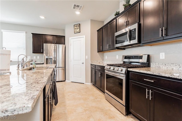 kitchen with visible vents, appliances with stainless steel finishes, a sink, dark brown cabinets, and light stone countertops