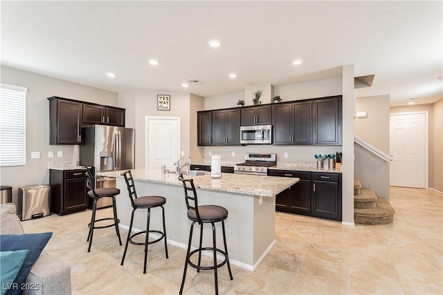 kitchen with a kitchen breakfast bar, a kitchen island with sink, stainless steel appliances, dark brown cabinets, and recessed lighting