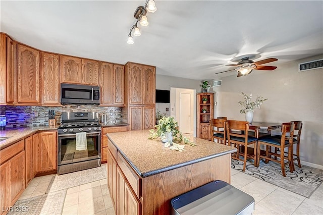 kitchen featuring a center island, light tile patterned floors, ceiling fan, stainless steel appliances, and decorative backsplash