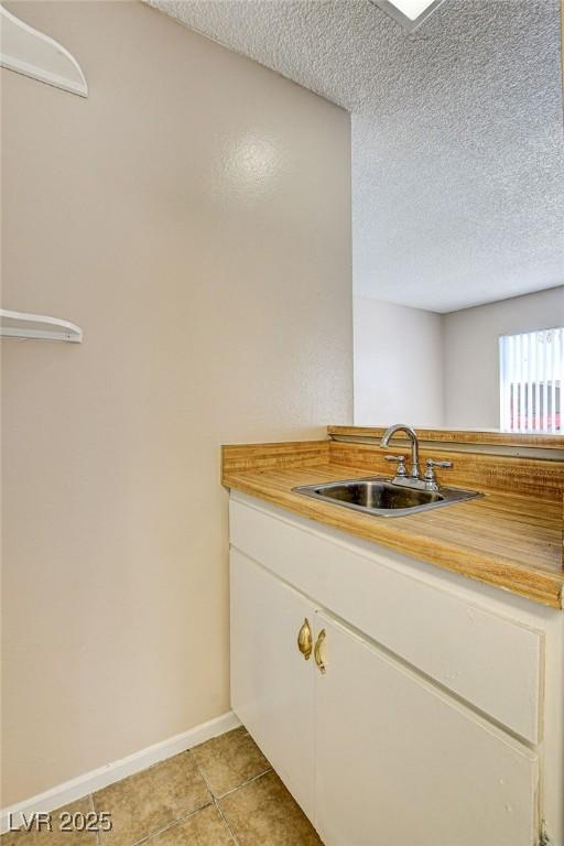 kitchen with white cabinetry, sink, a textured ceiling, and light tile patterned flooring