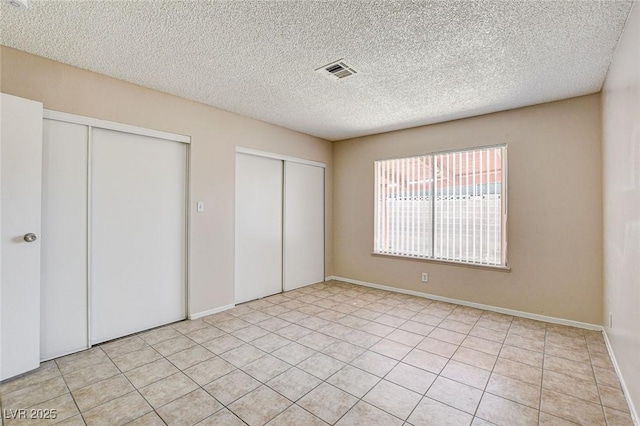 unfurnished bedroom with multiple closets, light tile patterned floors, and a textured ceiling