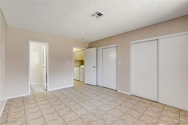 unfurnished bedroom with light tile patterned flooring, washing machine and dryer, a textured ceiling, and two closets