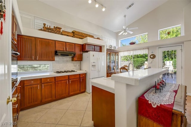 kitchen with a kitchen island, tasteful backsplash, white fridge with ice dispenser, light tile patterned floors, and stainless steel gas cooktop