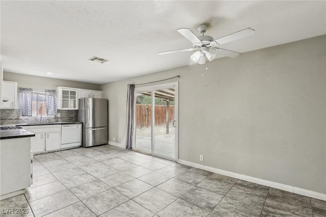 kitchen featuring stainless steel refrigerator, white cabinets, decorative backsplash, ceiling fan, and white dishwasher