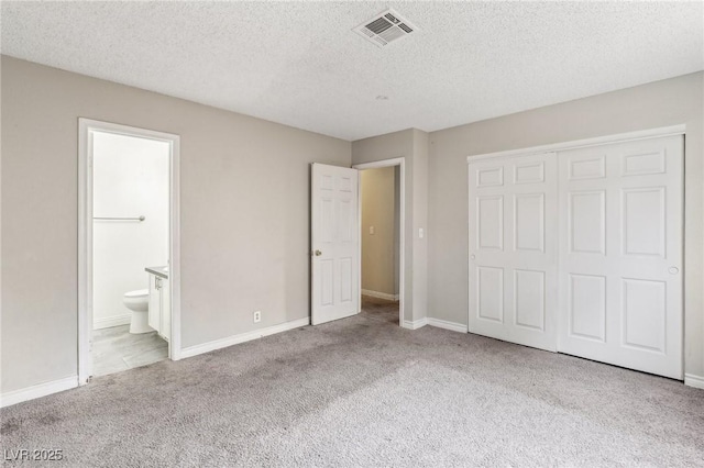 unfurnished bedroom featuring light carpet, a textured ceiling, ensuite bath, and a closet