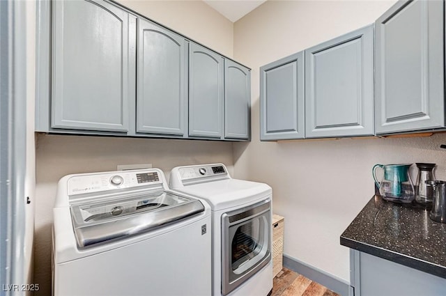 clothes washing area with cabinets, washing machine and clothes dryer, and light hardwood / wood-style floors