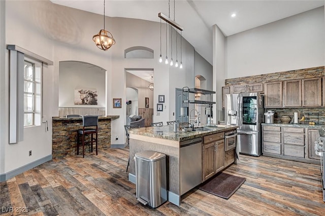 kitchen featuring appliances with stainless steel finishes, pendant lighting, sink, dark hardwood / wood-style flooring, and a center island with sink