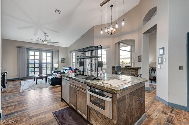 kitchen with sink, hardwood / wood-style flooring, appliances with stainless steel finishes, hanging light fixtures, and an island with sink