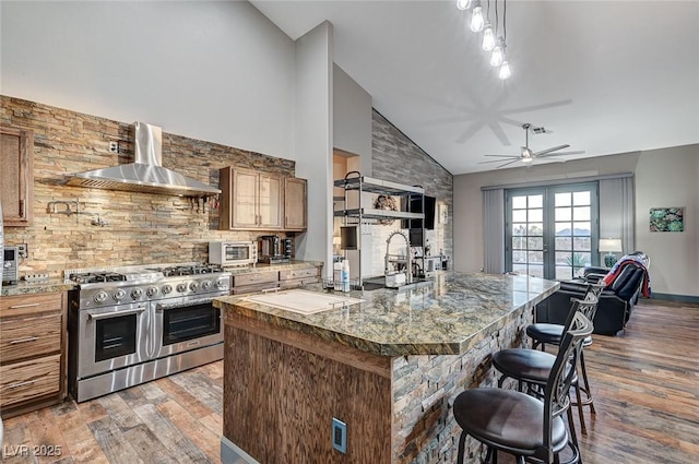 kitchen with a breakfast bar area, range with two ovens, wall chimney exhaust hood, light wood-type flooring, and french doors