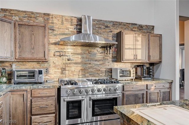 kitchen with wall chimney exhaust hood, high end stove, and backsplash