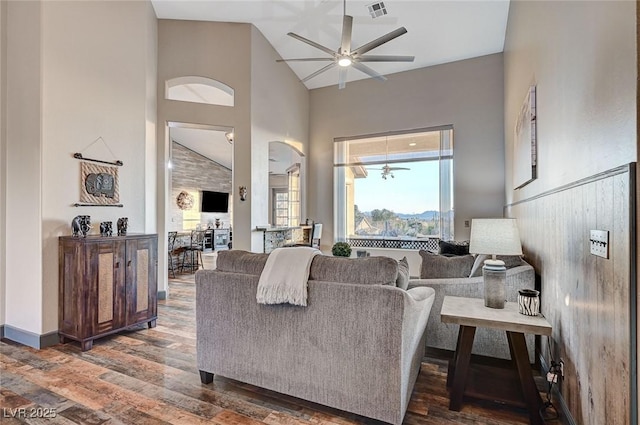 living room with dark wood-type flooring, ceiling fan, and high vaulted ceiling