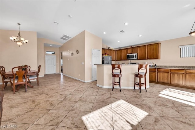 kitchen featuring pendant lighting, appliances with stainless steel finishes, a kitchen bar, and vaulted ceiling