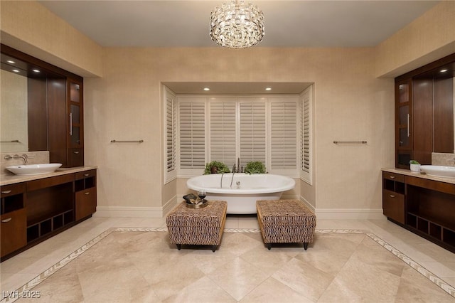 full bathroom with baseboards, a soaking tub, two vanities, a sink, and a chandelier