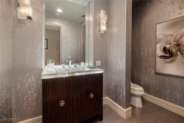 half bathroom featuring baseboards, toilet, vanity, and tile patterned flooring