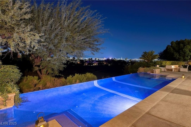 pool at night with an outdoor hangout area and a patio area