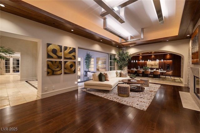 living area with a tray ceiling, arched walkways, hardwood / wood-style floors, and a fireplace