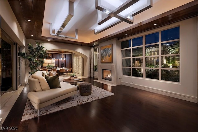 interior space with wood finished floors, a fireplace with flush hearth, recessed lighting, arched walkways, and a raised ceiling