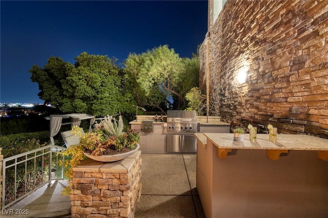 patio at night featuring exterior kitchen and area for grilling